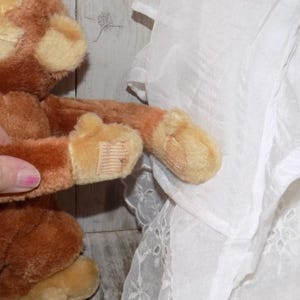 May include: A plush brown monkey with tan accents. The monkey's arm is extended, revealing a tan paw with a small tag. The plush toy is soft and cuddly, perfect for children.