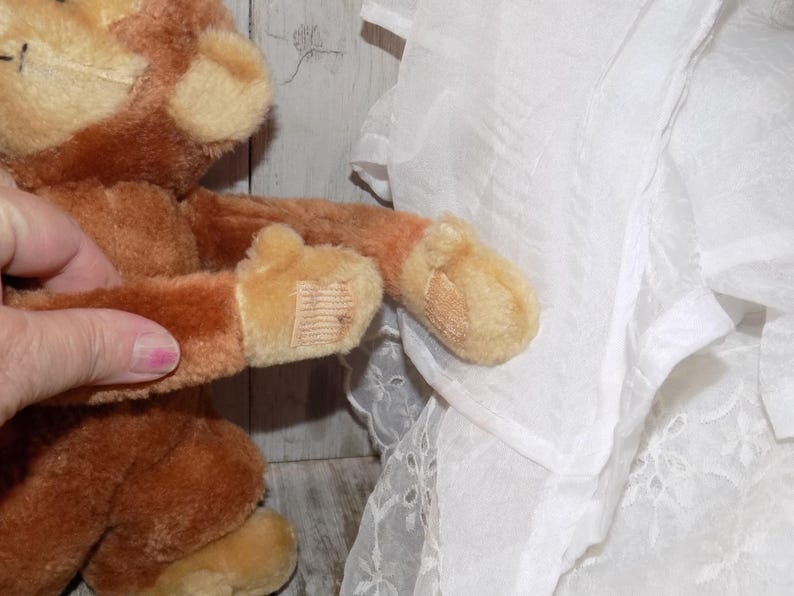 May include: A plush brown monkey with tan accents. The monkey's arm is extended, revealing a tan paw with a small tag. The plush toy is soft and cuddly, perfect for children.