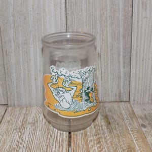 May include: A clear glass jar with a cartoon image of a Tasmanian devil falling from a tree. The image is on a yellow background with green accents.