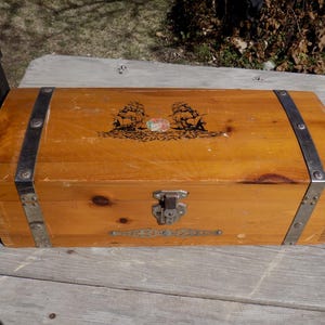 May include: A wooden treasure chest with a hinged lid and metal accents. The lid features a design of two ships with a globe in the center.