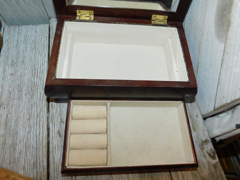 May include: A dark wood jewelry box with a hinged lid and a mirror inside. The box has a removable tray with ring rolls.