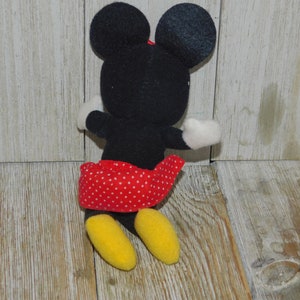 May include: A black and red plush toy of Minnie Mouse. She is wearing a red skirt with white polka dots and has yellow shoes.
