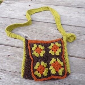 May include: A crocheted shoulder bag with a green strap and a brown, orange, and green patterned front. The bag is made of granny squares.