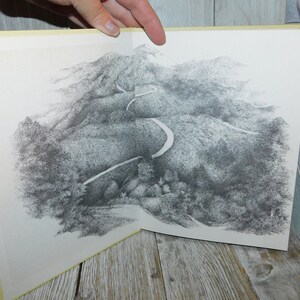 May include: A black and white drawing of a winding road through a mountainous landscape. The road is depicted in detail, with curves and turns visible. The mountains are shown as a series of hills and valleys, with trees and foliage scattered throughout.