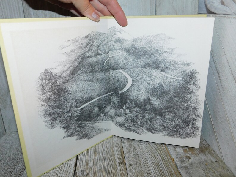 May include: A black and white drawing of a winding road through a mountainous landscape. The road is depicted in detail, with curves and turns visible. The mountains are shown as a series of hills and valleys, with trees and foliage scattered throughout.