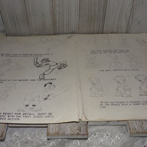 May include: Vintage open book with pencil sketches of cartoon character construction. The pages show step-by-step instructions, including establishing a line of action and roughing in masses and features. The text includes instructions on how to draw the characters.