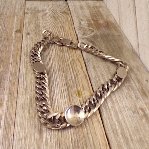 May include: A silver chain necklace with three round silver charms. The chain is a curb link style.