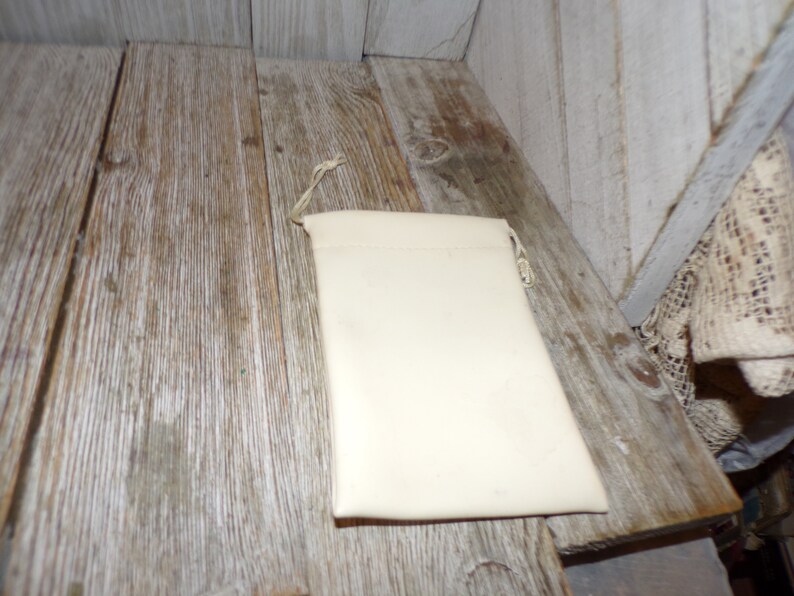 Puede incluir: Una bolsa blanca de cord&oacute;n con un dise&ntilde;o sencillo, hecha de una tela suave. La bolsa est&aacute; sobre una superficie de madera.