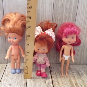 Pode incluir: Tr&ecirc;s bonecas vintage Strawberry Shortcake. As bonecas medem aproximadamente 15 cm de altura e t&ecirc;m cabelo vermelho, rosa e loiro. As bonecas usam roupas diferentes, incluindo um vestido rosa e branco, um vestido xadrez rosa e branco e uma fralda branca.