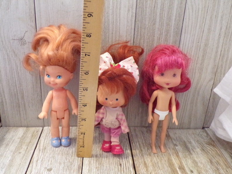 Pode incluir: Tr&ecirc;s bonecas vintage Strawberry Shortcake. As bonecas medem aproximadamente 15 cm de altura e t&ecirc;m cabelo vermelho, rosa e loiro. As bonecas usam roupas diferentes, incluindo um vestido rosa e branco, um vestido xadrez rosa e branco e uma fralda branca.