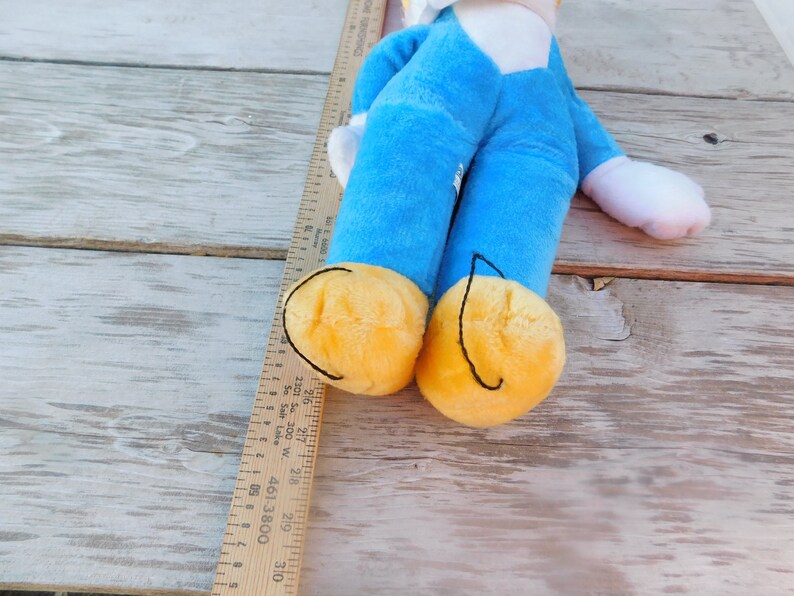 May include: A blue plush toy with yellow feet and a white face. The toy is lying on a wooden surface.