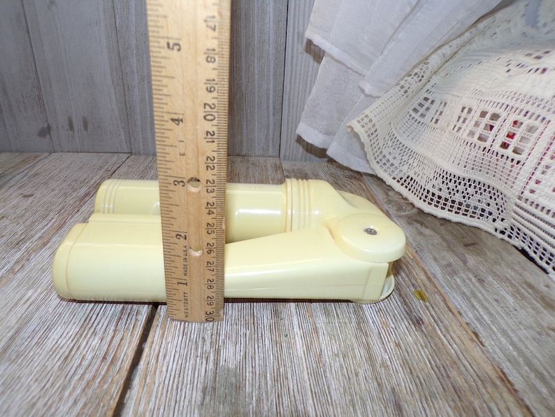 May include: A pair of vintage off-white plastic hair curlers, measuring approximately 7 inches in length, are displayed on a wooden surface. The curlers are designed with a rounded shape and a textured surface.