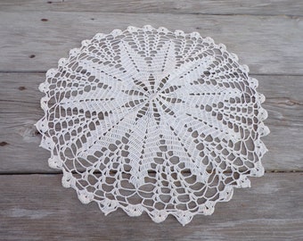 May include: White crocheted doily with a delicate floral pattern. The doily is circular and has a scalloped edge.