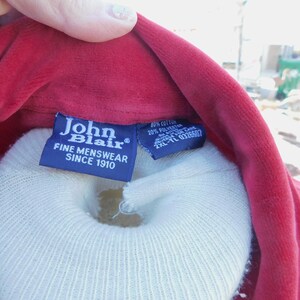 May include: A red velvet shirt with a blue label that reads "John Blair Fine Menswear Since 1910". A white care label is attached to the shirt with the text "40% Cotton 20% Polyester Made in Canada 2XL-TL 0326507".