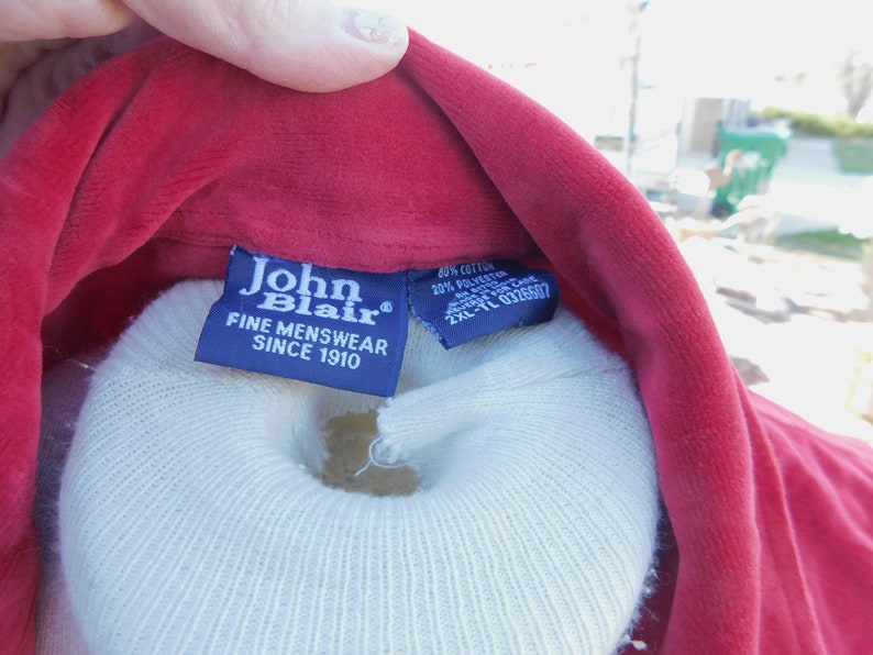 May include: A red velvet shirt with a blue label that reads "John Blair Fine Menswear Since 1910". A white care label is attached to the shirt with the text "40% Cotton 20% Polyester Made in Canada 2XL-TL 0326507".