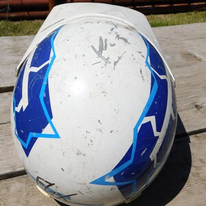 May include: White motorcycle helmet with blue and light blue geometric designs. The helmet has visible scratches and dirt.