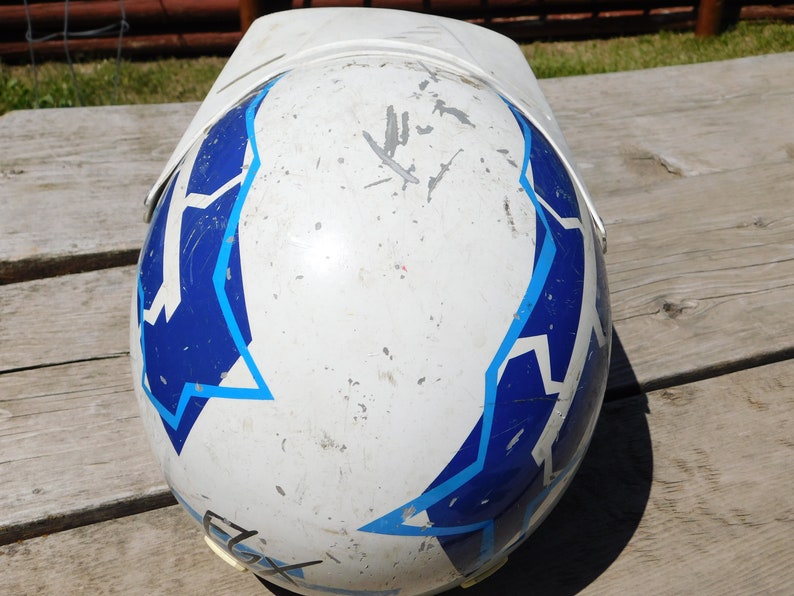 May include: White motorcycle helmet with blue and light blue geometric designs. The helmet has visible scratches and dirt.
