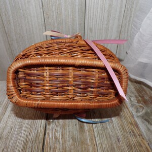 Peut inclure: Un panier en osier tress&eacute; avec un ruban rose nou&eacute; autour de la poign&eacute;e. Le panier est brun et a une finition naturelle.