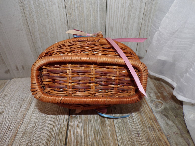 Peut inclure: Un panier en osier tress&eacute; avec un ruban rose nou&eacute; autour de la poign&eacute;e. Le panier est brun et a une finition naturelle.