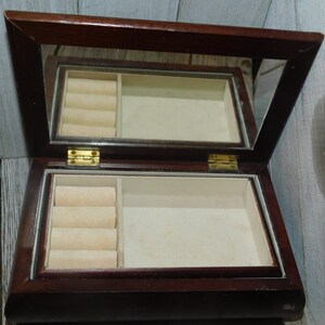 May include: A dark wood jewelry box with a mirrored lid and a velvet interior. The box has a ring holder with four slots.