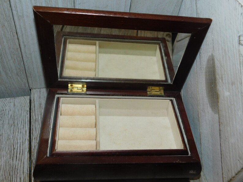 May include: A dark wood jewelry box with a mirrored lid and a velvet interior. The box has a ring holder with four slots.