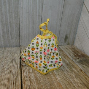May include: A white bib with a yellow trim and a floral pattern in pink, orange, and green. The bib has a tie closure.