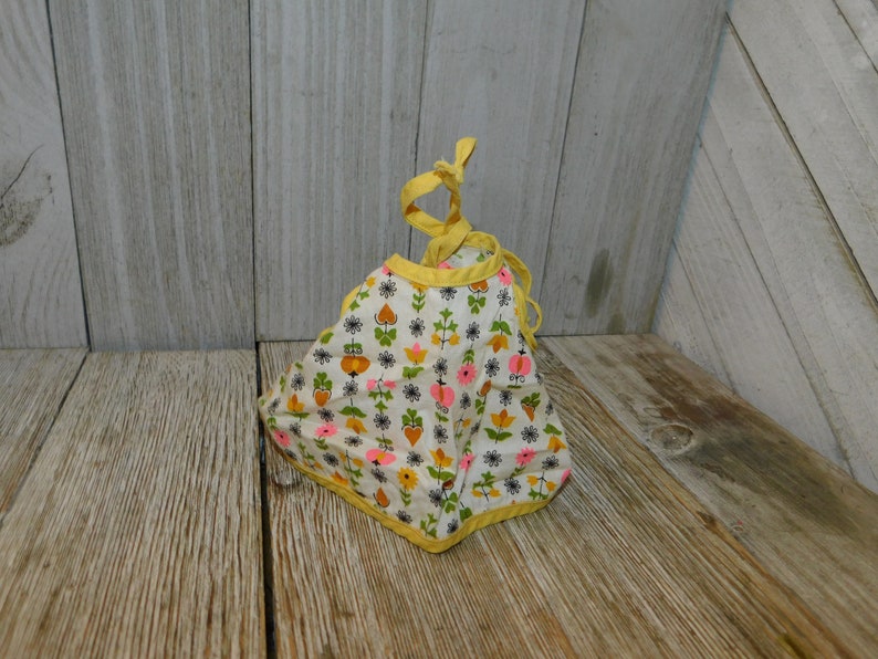 May include: A white bib with a yellow trim and a floral pattern in pink, orange, and green. The bib has a tie closure.