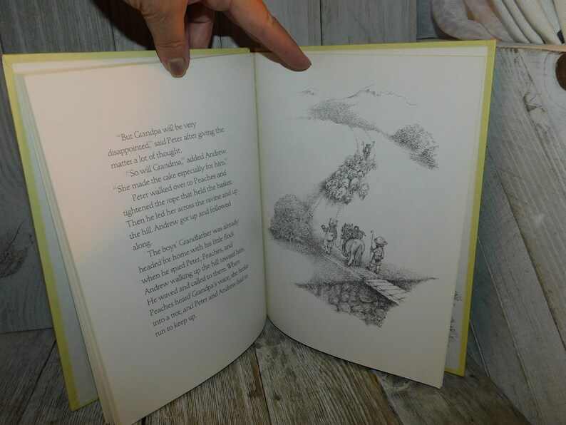 May include: A black and white illustration of a group of children walking along a path. The children are carrying a large cake and a rope. The text in the image reads, "But Grandpa will be very disappointed," said Peter after giving the matter a lot of thought. "So will Grandma," added Andrew. She made the cake especially for him. Peter walked over to Peaches and tightened the rope that held the basket. Then he led her across the ravine and up the hill. Andrew got up and followed along. The boys' Grandfather was already headed for home with his little flock when he spied Peter, Peaches, and Andrew walking up the hill toward him. He waved and called to them. When Peaches heard Grandpa's voice, she broke into a trot, and Peter and Andrew had to run to keep up."