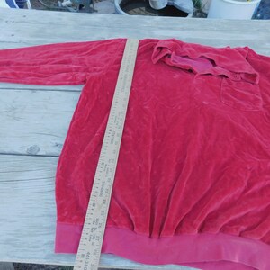May include: A red long-sleeved shirt with a collared neckline and a button closure. The shirt has a pocket on the left side and a ribbed hem.