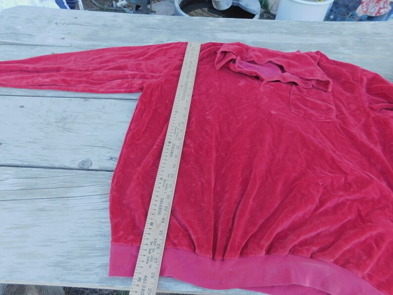 May include: A red long-sleeved shirt with a collared neckline and a button closure. The shirt has a pocket on the left side and a ribbed hem.