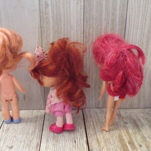 Pode incluir: Tr&ecirc;s bonecas com cabelo vermelho. A boneca &agrave; esquerda est&aacute; nua e usa sapatos azuis. A boneca do meio est&aacute; usando um vestido rosa e sapatos rosa. A boneca &agrave; direita est&aacute; usando um mai&ocirc; branco e tem cabelo rosa.
