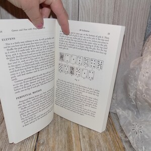 May include: A book titled "Games and Fun with Playing Cards" with an open page showing a card game called "Elevens" and a card game called "Solitaires". The page shows the rules for the games and a diagram of the card layout for the "Solitaires" game.