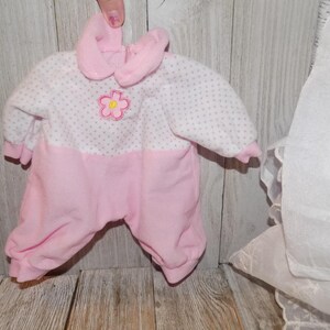May include: Pink and white baby onesie with a white flower design. The onesie has a pink collar and long sleeves.