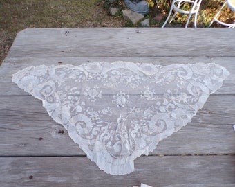 May include: A white lace shawl with a delicate floral pattern. The shawl is made of a fine, sheer fabric and has a scalloped edge.