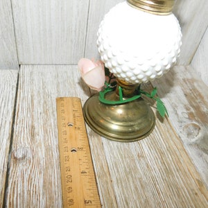 May include: White milk glass oil lamp with a gold base and green leaves. The lamp has a white rose on the side.