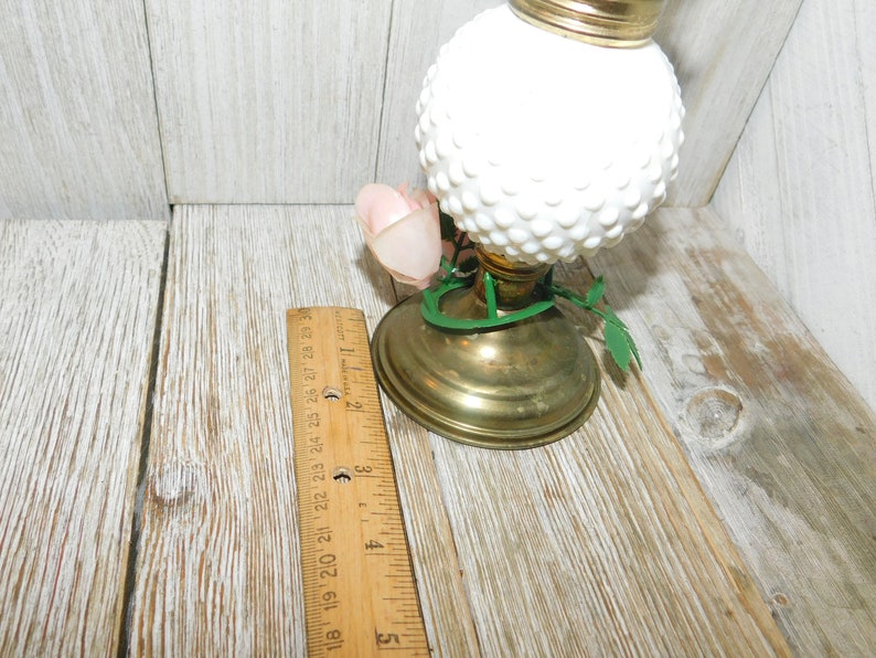 May include: White milk glass oil lamp with a gold base and green leaves. The lamp has a white rose on the side.