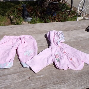 Puede incluir: Un conjunto de beb&eacute; rosa con una chaqueta con capucha y pantalones. La chaqueta tiene un dise&ntilde;o floral y los pantalones tienen un dise&ntilde;o de mariposa.