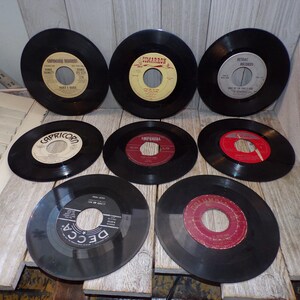 May include: A collection of eight black vinyl 45 RPM records with various center labels including Capricorn, Cimarron, Retrac, Imperial, and Decca. The records are arranged in three rows, featuring circular paper labels in colors like yellow, white, red, and black.