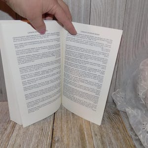 May include: Open book with a white cover and black text. The book is titled "Catalog of Editions" and lists various books and their authors. The right page of the book is titled "Crown of Thorns Breed" and lists various books and their authors.