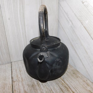 May include: A black metal tea kettle with a wooden handle. The kettle has a dented and worn appearance.