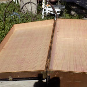 May include: An open, antique trunk with a light brown exterior and a patterned interior. The trunk is made of wood and metal, with visible hinges and clasps. The interior lining features a striped pattern in shades of beige and red.