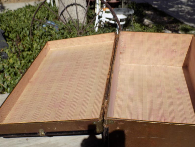 May include: An open, antique trunk with a light brown exterior and a patterned interior. The trunk is made of wood and metal, with visible hinges and clasps. The interior lining features a striped pattern in shades of beige and red.