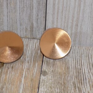 May include: Two round, copper-colored drawer knobs with a raised, circular design in the center.