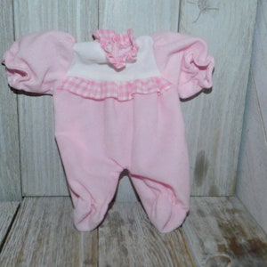 May include: A pink baby doll onesie with white and pink gingham trim and a white ruffle collar.