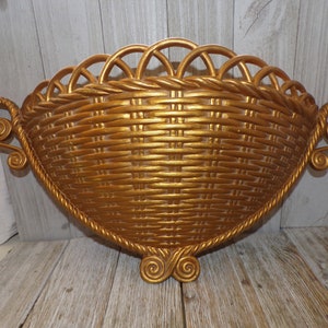May include: A gold-colored, half-round wall-mounted basket with a woven design and decorative scrollwork on the handles.
