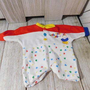 May include: A white, red, yellow, and blue baby onesie with a colorful heart pattern. The onesie has the text "Let's Play Tag..." and a cartoon bear wearing a blue shirt and yellow shorts.