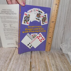 May include: A purple book titled "Games and Fun with Playing Cards" by Joseph Leeming. The cover features illustrations of playing cards, including hearts, spades, and numbered cards.