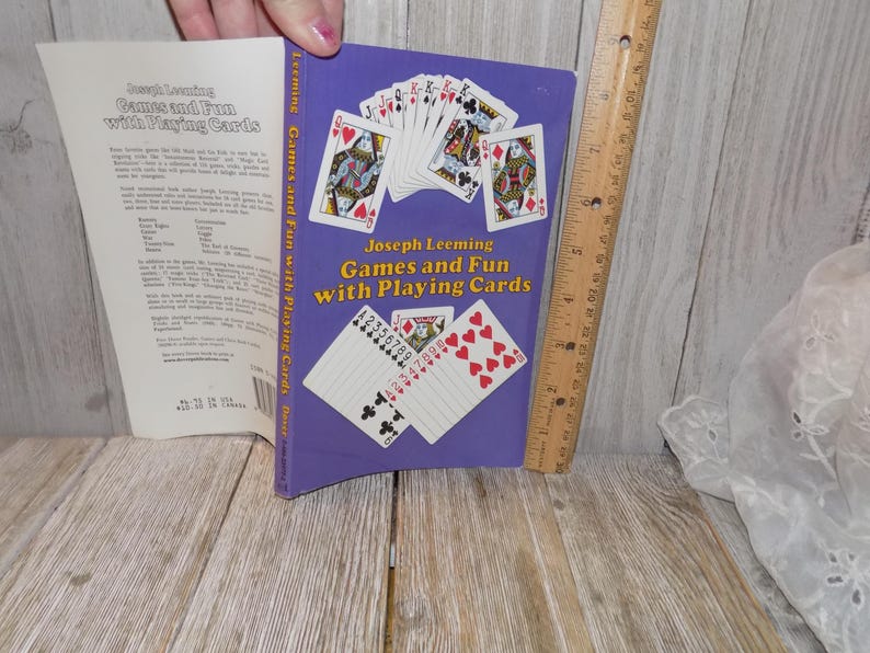 May include: A purple book titled "Games and Fun with Playing Cards" by Joseph Leeming. The cover features illustrations of playing cards, including hearts, spades, and numbered cards.