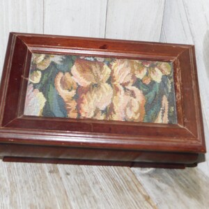 May include: A wooden box with a hinged lid. The lid is decorated with a floral tapestry featuring a colorful floral pattern. The box is a dark brown color.