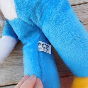 May include: Blue and white plush toy eagle with a yellow beak and feet. The toy has a tag that reads "ACE Novelty Co., Inc. Niles, Chicago, Seattle."